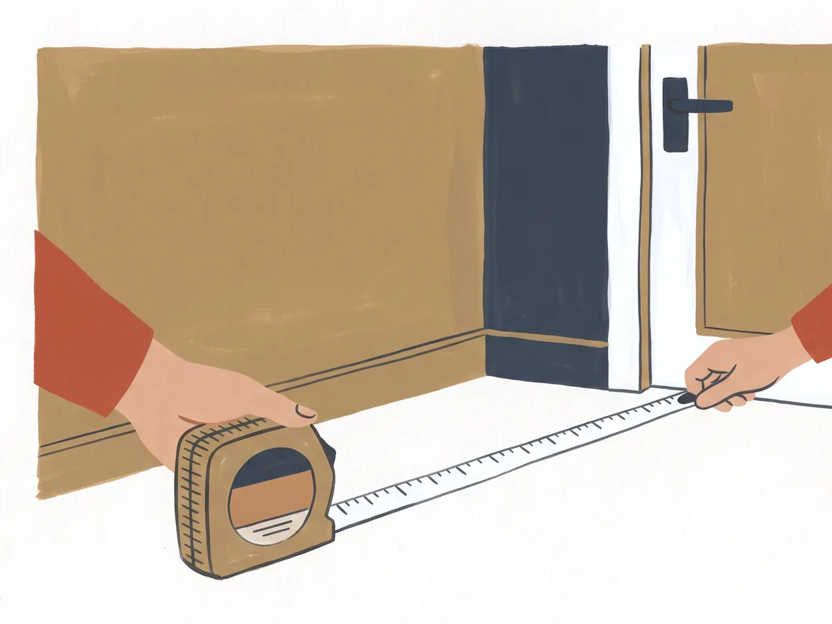 Two hands pulling a tape measure along the bottom of a wall toward a door frame